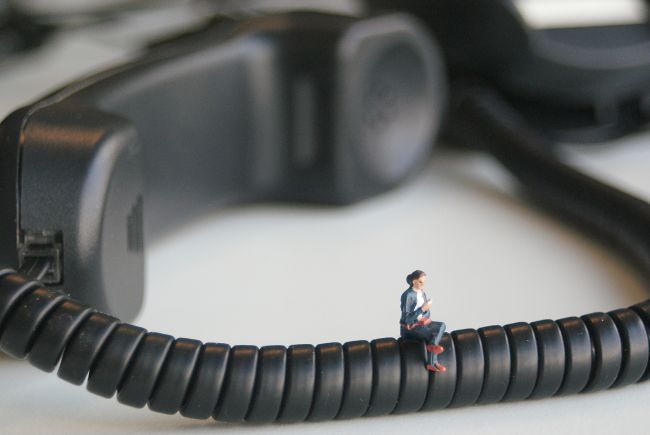 Small model figure sitting on telephone handset cable