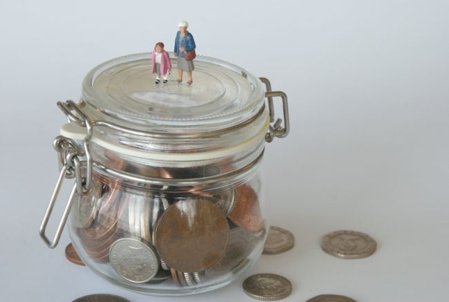 Small model figures standing on glass jar filled with coins