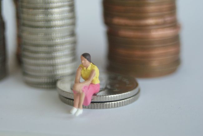 Small model figure sitting beside large pile of coins