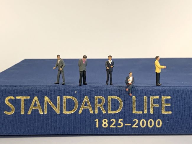 Small model figures standing on a book titled Standard Life