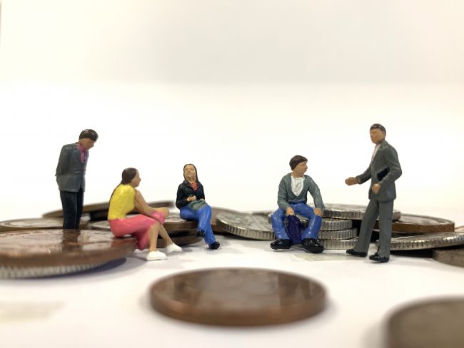 Small model figures sitting around small piles of coins